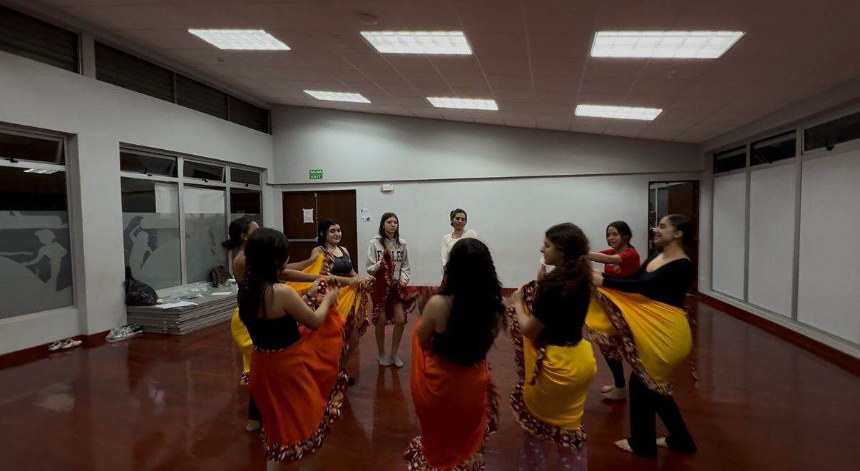 Mujeres jóvenes en círculo bailando con enaguas, en un aula
